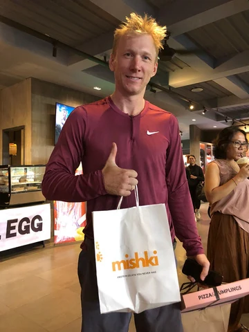 A smiling athlete holding a Mishki bag and giving a thumbs up